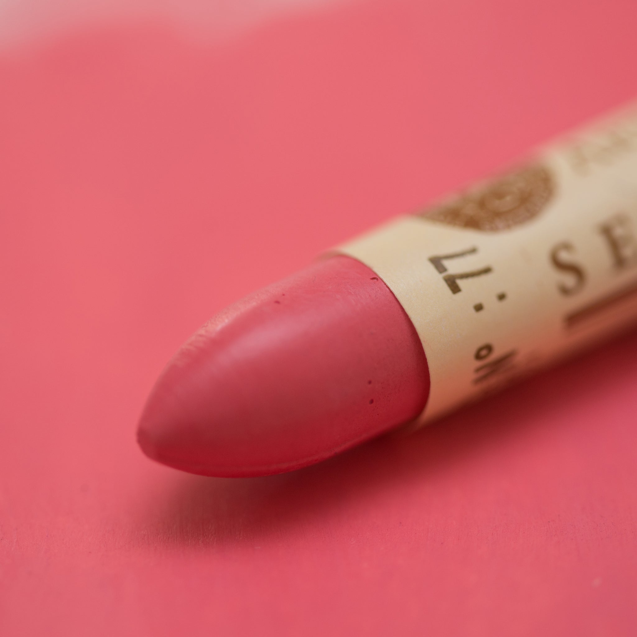 A close-up of a Sennelier oil pastel on a pink background.