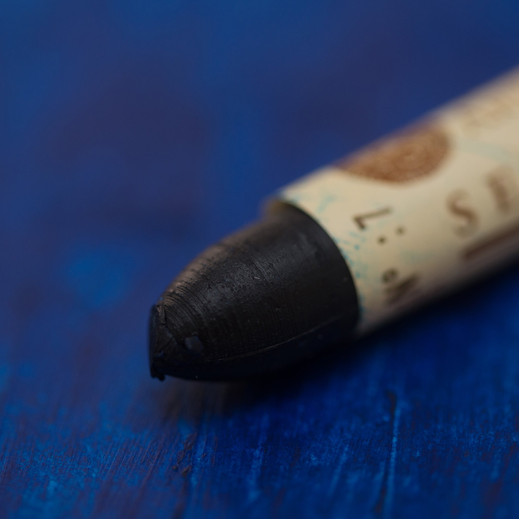 A close-up of a Sennelier oil pastel on a blue background.