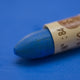 A close-up of a Sennelier oil pastel on a blue background.