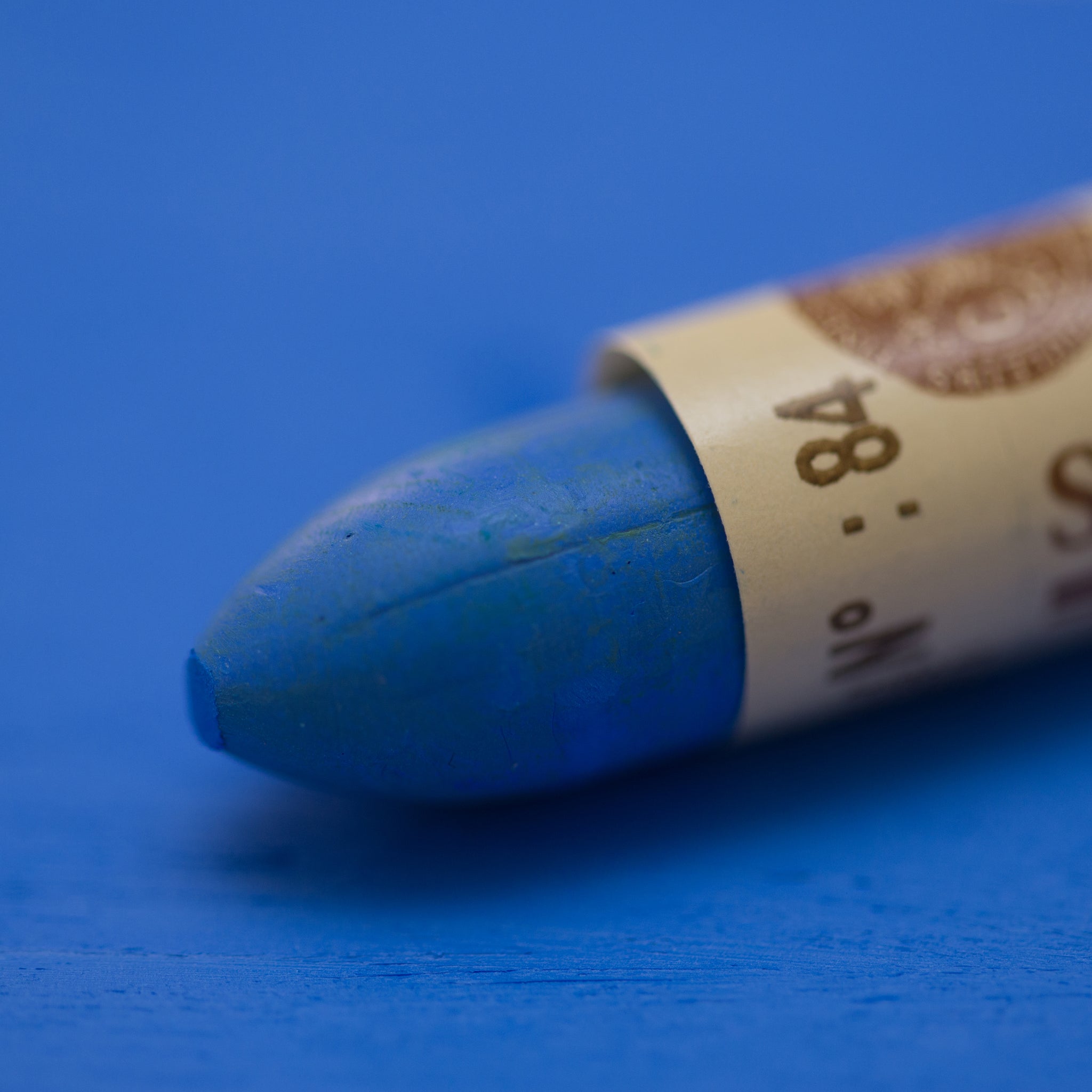 A close-up of a Sennelier oil pastel on a blue background.