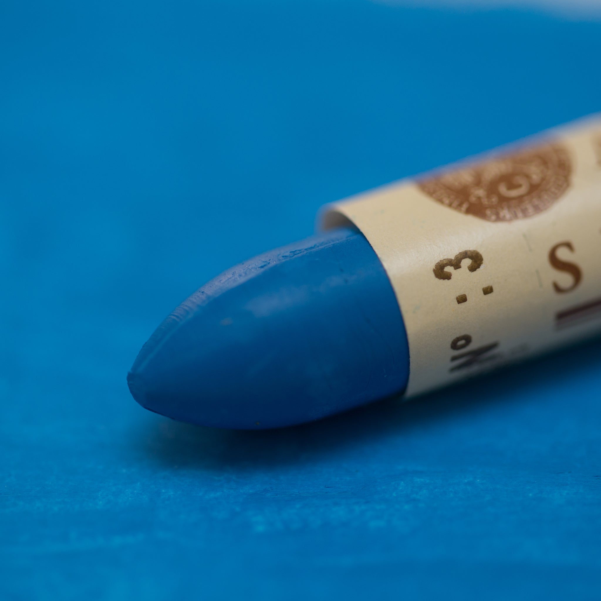A close-up of a Sennelier oil pastel on a blue background.