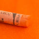 A close-up of an Orange Sennelier extra soft pastel. on the same coloured background, with the colour information printed on the paper wrap.