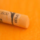 A close-up of an Orange Sennelier extra soft pastel. on the same coloured background, with the colour information printed on the paper wrap.