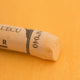 A close-up of an Orange Sennelier extra soft pastel. on the same coloured background, with the colour information printed on the paper wrap.