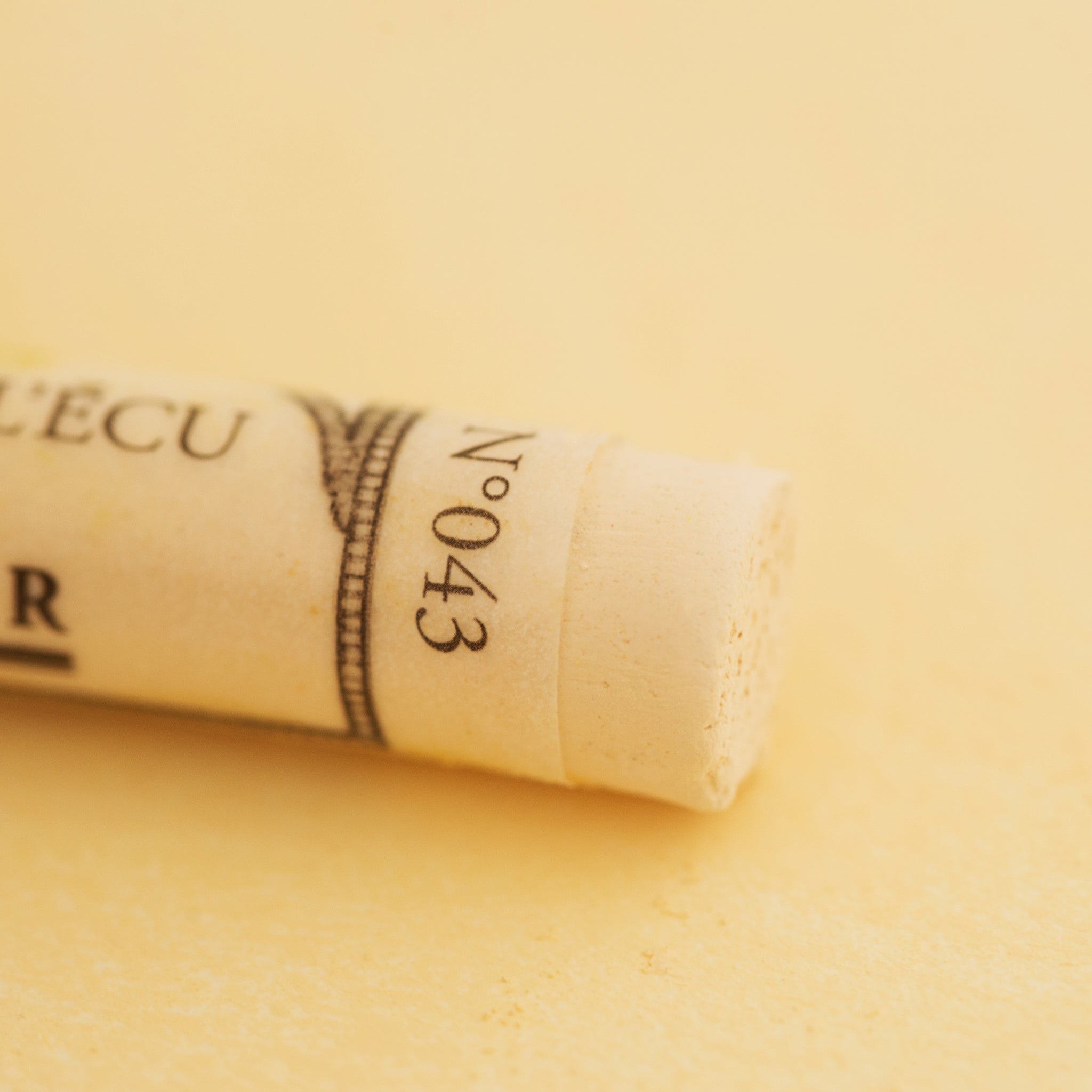 A close-up of a pale Orange Sennelier extra soft pastel. on the same coloured background, with the colour information printed on the paper wrap.