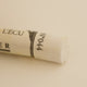 A close-up of a white Sennelier extra soft pastel. on the same coloured background, with the colour information printed on the paper wrap.