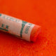 A close-up of an orange Sennelier extra soft pastel on the same coloured background, with the colour information printed on the paper wrap.