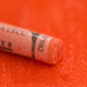 A close-up of an orange Sennelier extra soft pastel on the same coloured background, with the colour information printed on the paper wrap.