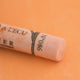 A close-up of a pale orange Sennelier extra soft pastel on the same coloured background, with the colour information printed on the paper wrap.