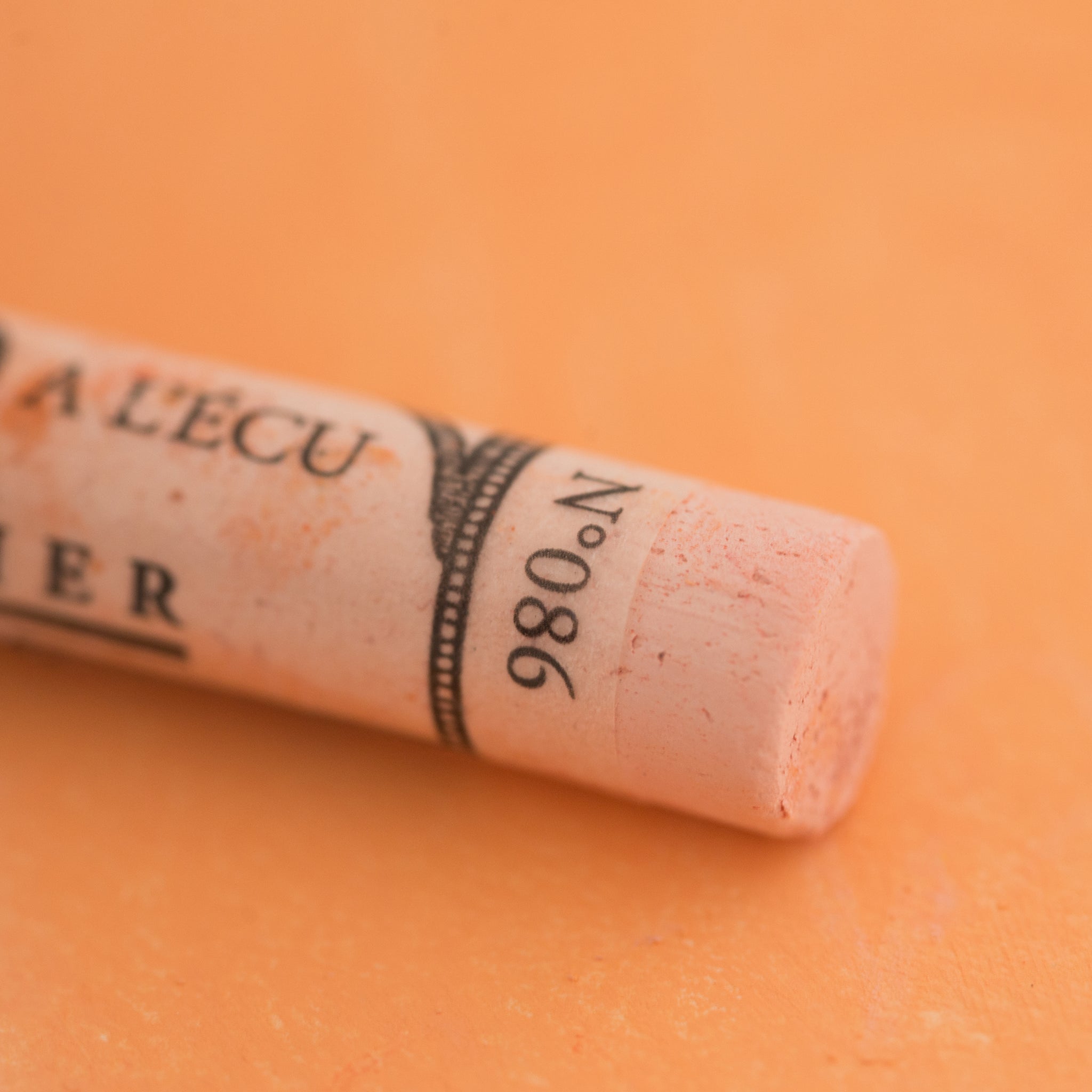 A close-up of a pale orange Sennelier extra soft pastel on the same coloured background, with the colour information printed on the paper wrap.