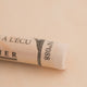 A close-up of a white Sennelier extra soft pastel on the same coloured background, with the colour information printed on the paper wrap.