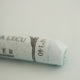   A close-up of a white Sennelier extra soft pastel on the same coloured background, with the colour information printed on the paper wrap.