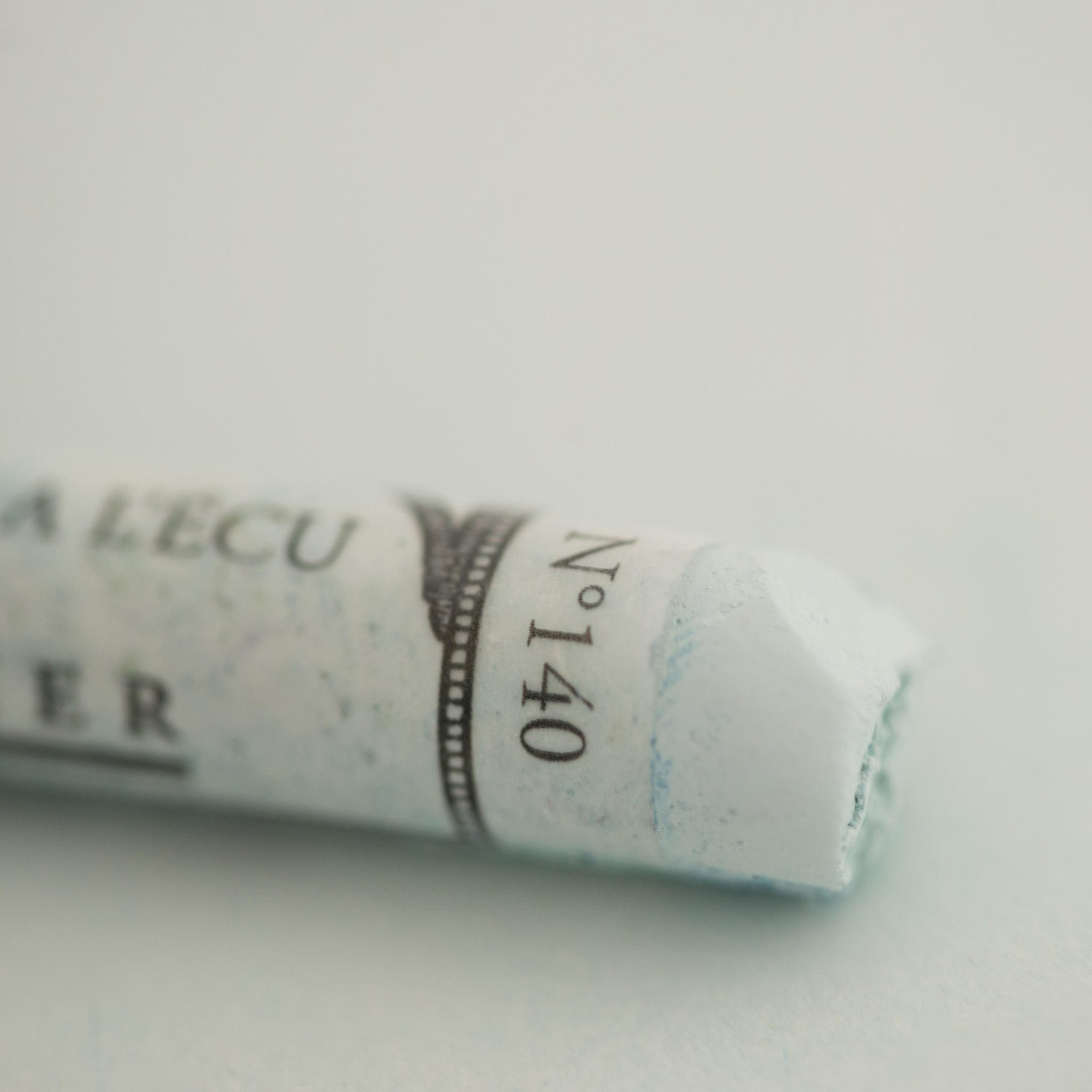   A close-up of a white Sennelier extra soft pastel on the same coloured background, with the colour information printed on the paper wrap.