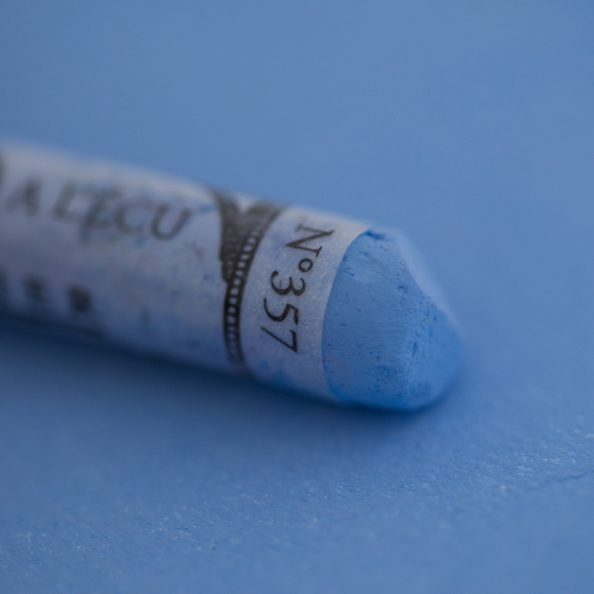  A close-up of a blue Sennelier extra soft pastel on the same coloured background, with the colour information printed on the paper wrap.