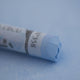 A close-up of a light blue Sennelier extra soft pastel on the same coloured background, with the colour information printed on the paper wrap.