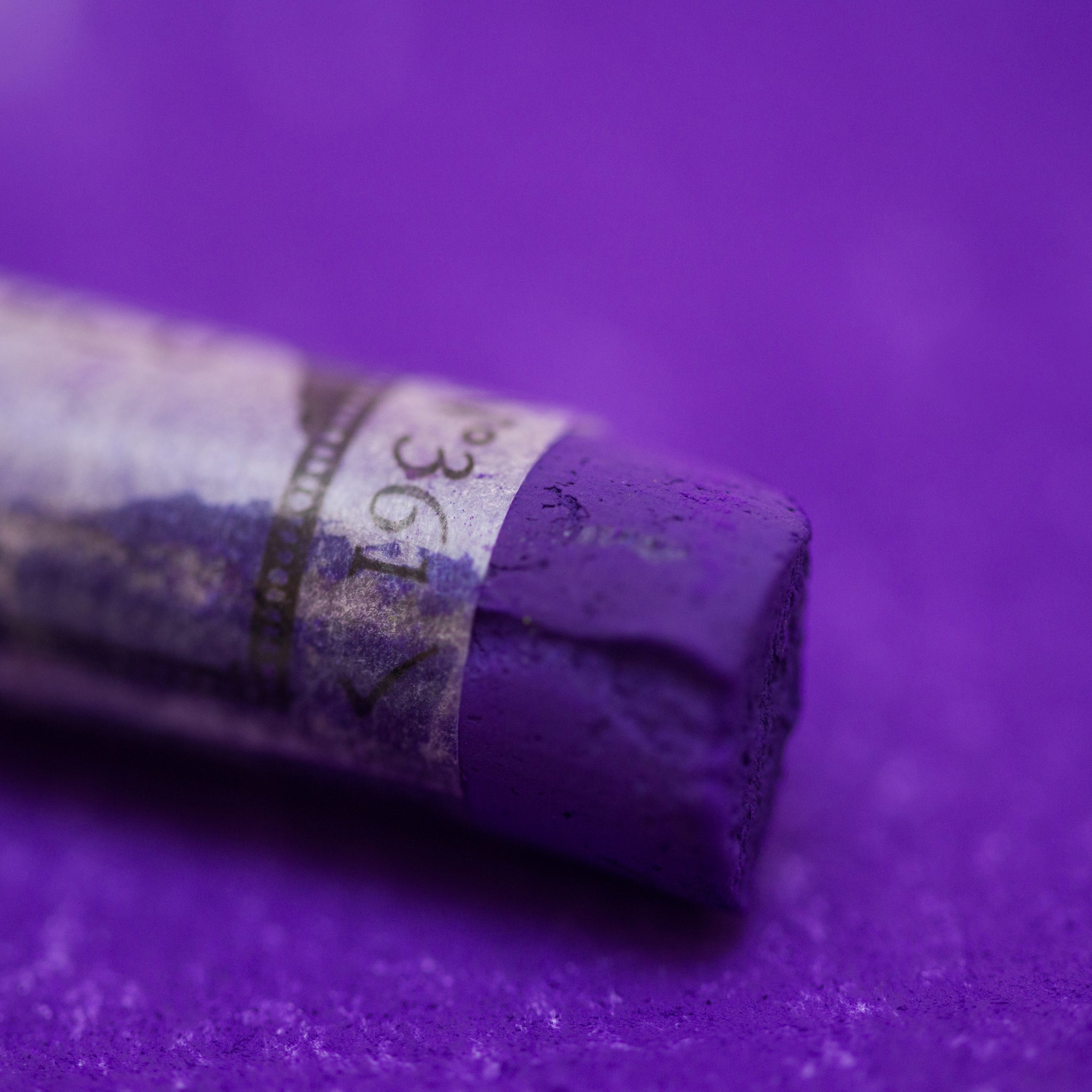  A close-up of a purple Sennelier extra soft pastel on the same coloured background, with the colour information printed on the paper wrap.