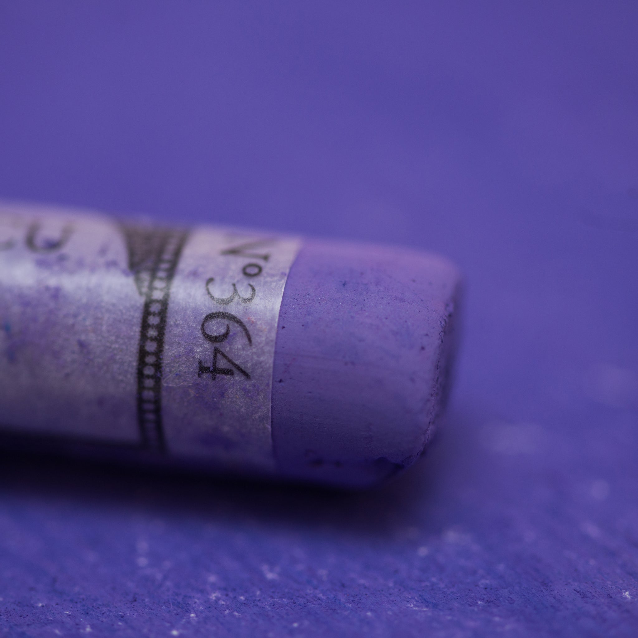  A close-up of a purple Sennelier extra soft pastel on the same coloured background, with the colour information printed on the paper wrap.