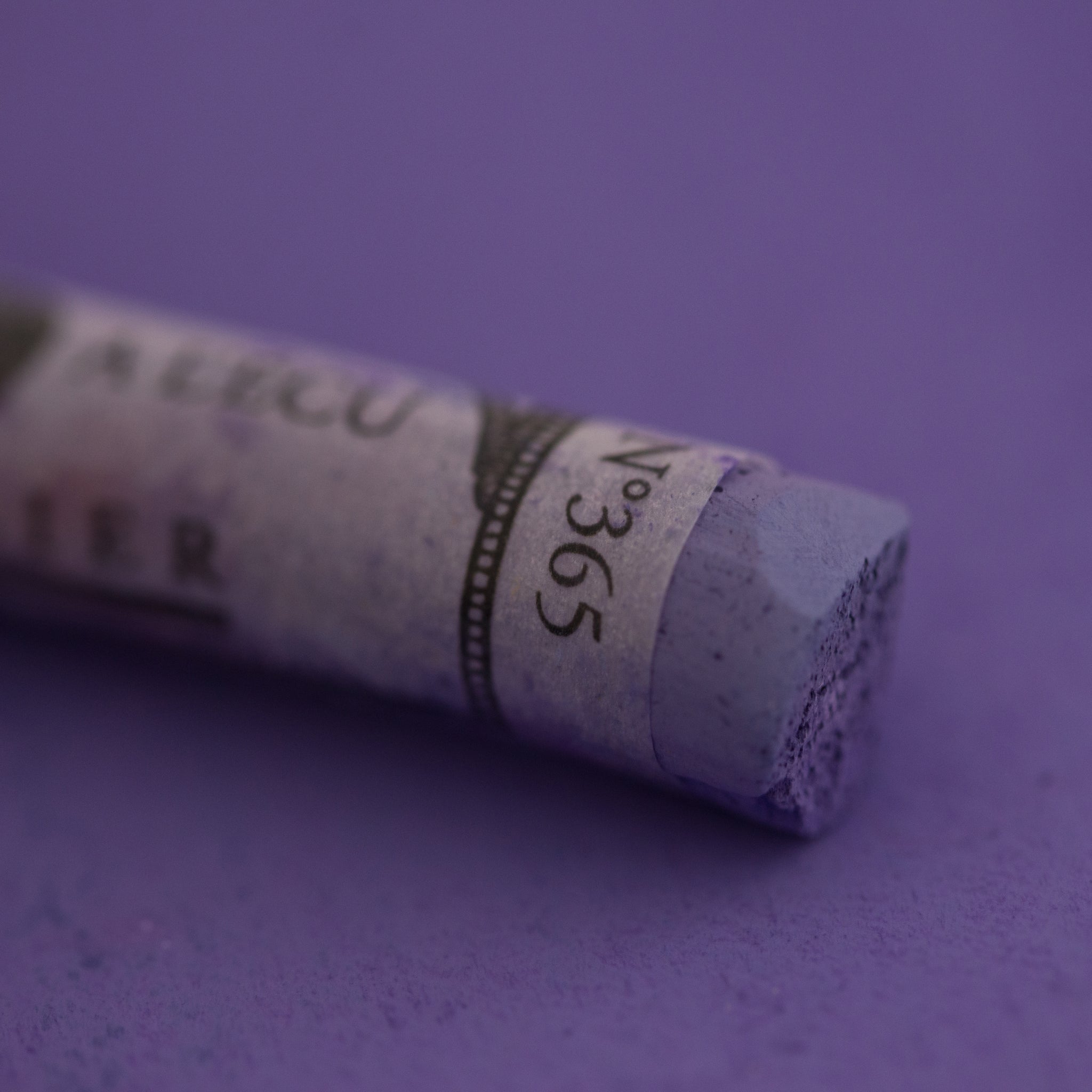  A close-up of a purple Sennelier extra soft pastel on the same coloured background, with the colour information printed on the paper wrap.