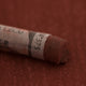 A close-up of a red-brown Sennelier extra soft pastel on the same coloured background, with the colour information printed on the paper wrap.