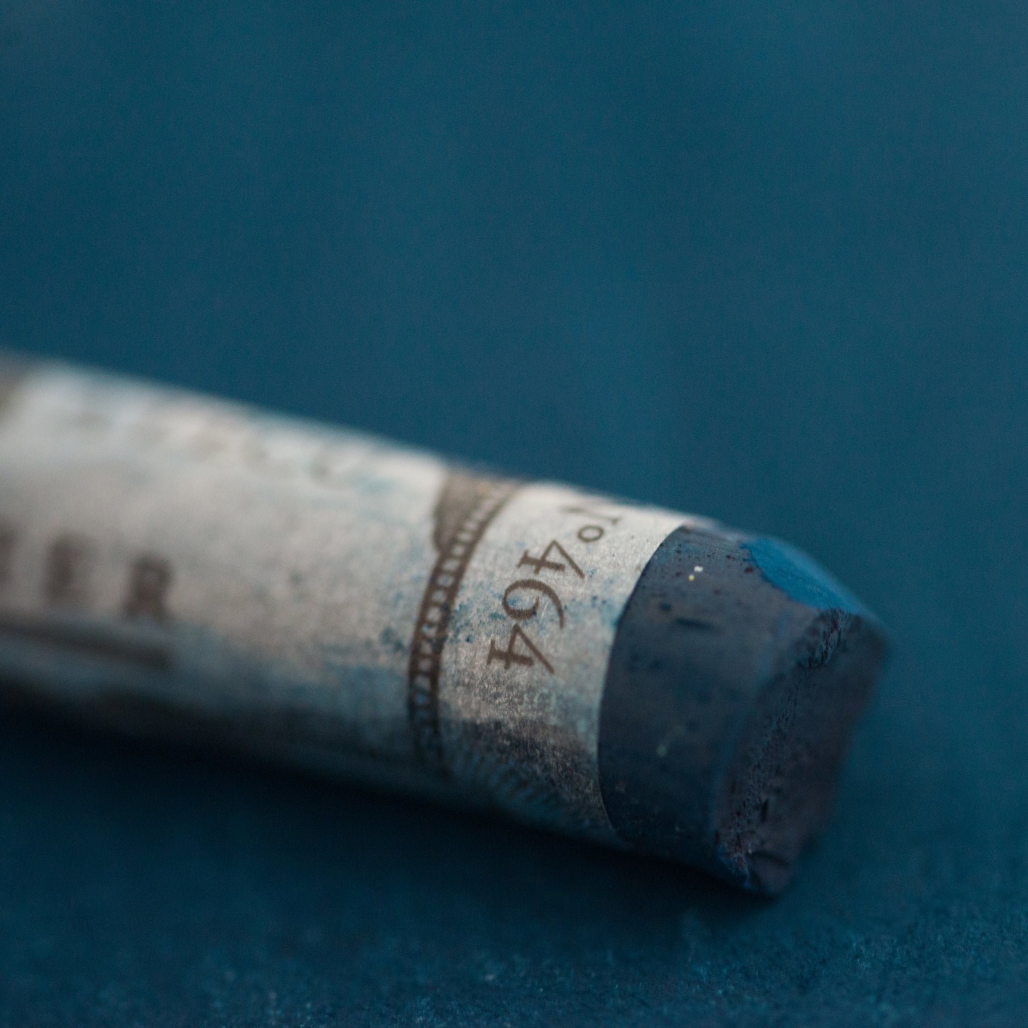  A close-up of a blue Sennelier extra soft pastel on the same coloured background, with the colour information printed on the paper wrap.