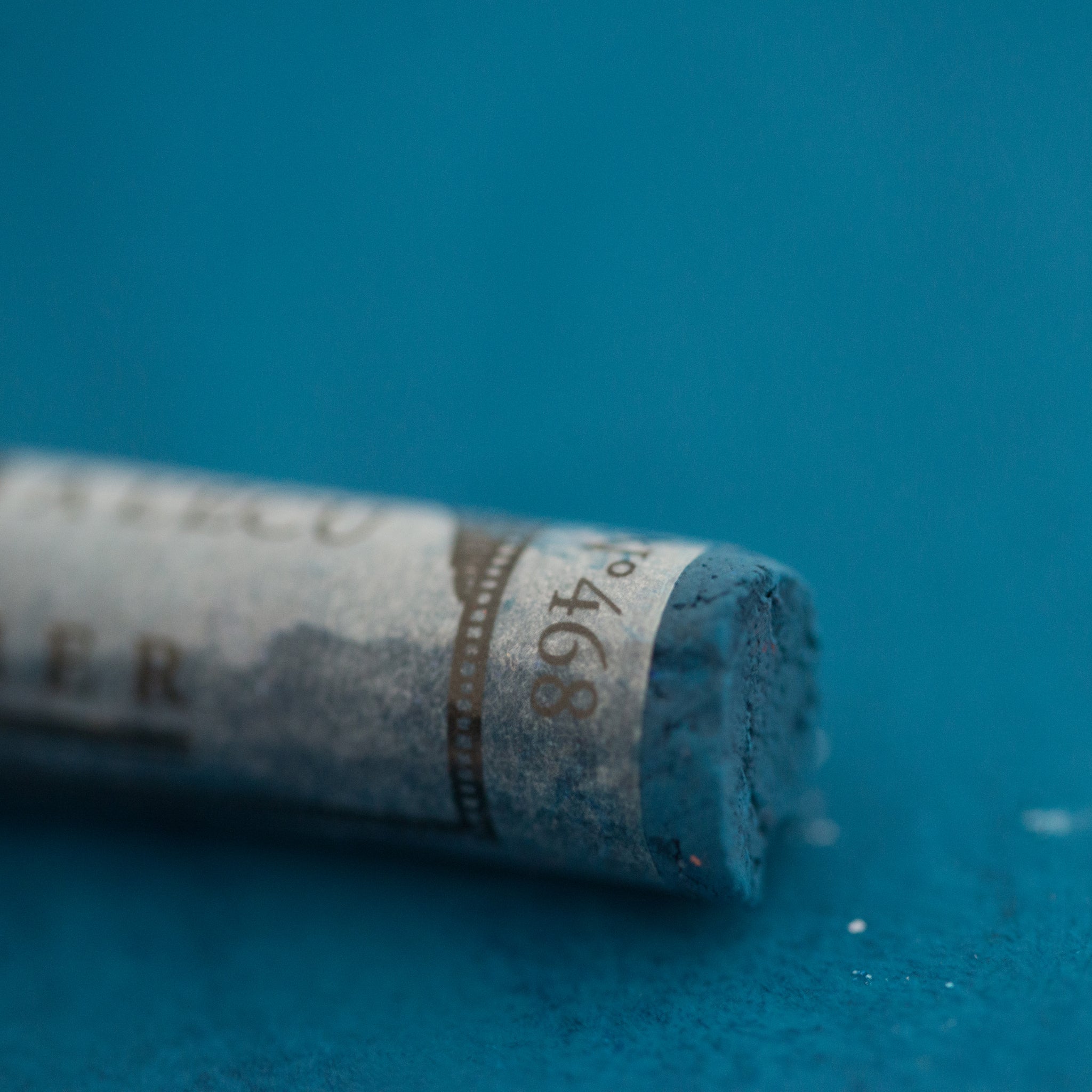  A close-up of a blue Sennelier extra soft pastel on the same coloured background, with the colour information printed on the paper wrap.