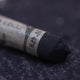 A close-up of a dark grey Sennelier extra soft pastel. on the same coloured background, with the colour information printed on the paper wrap.