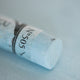 A close-up of a light blue Sennelier extra soft pastel. on the same coloured background, with the colour information printed on the paper wrap.