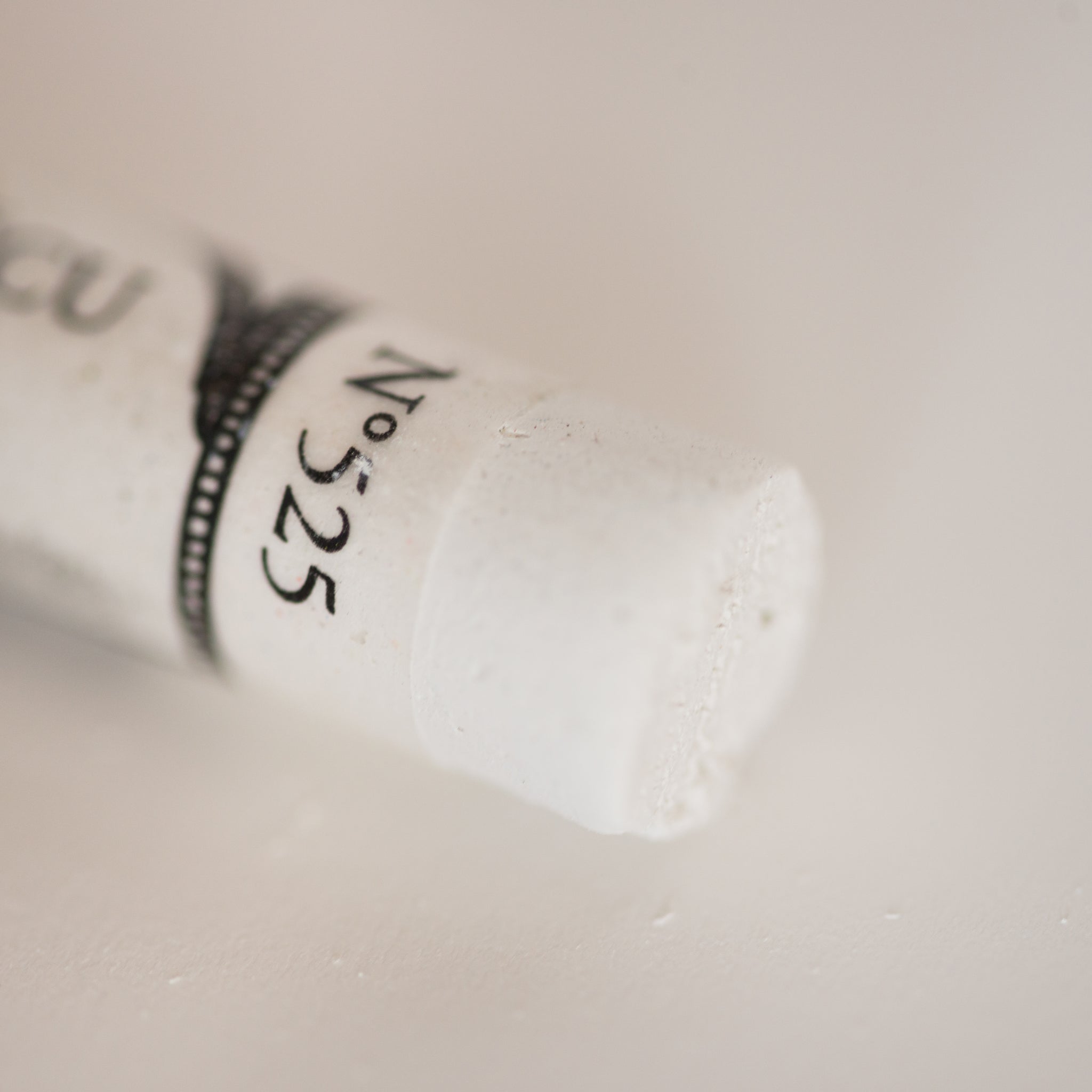 A close-up of a white Sennelier extra soft pastel. on the same coloured background, with the colour information printed on the paper wrap.