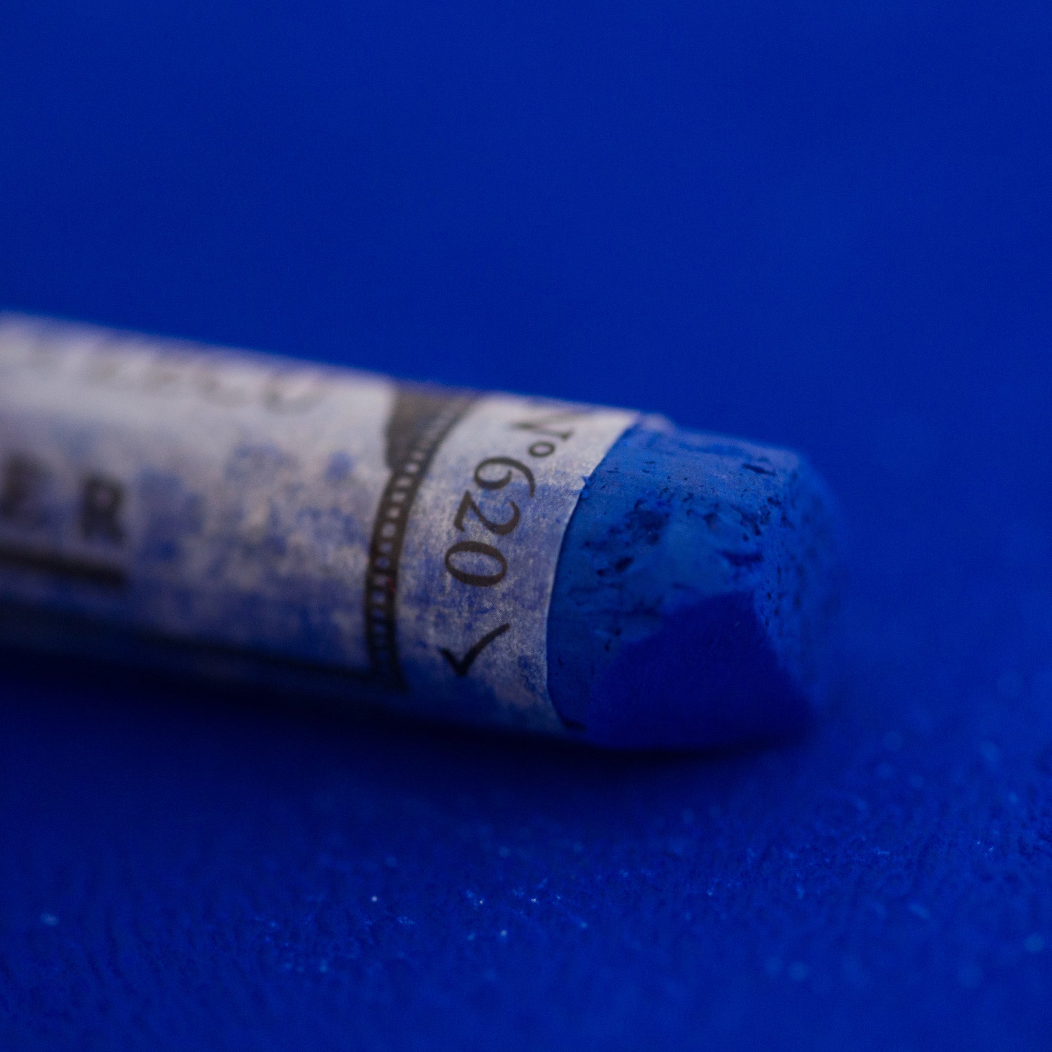  A close-up of a vibrant blue Sennelier extra soft pastel on the same coloured background, with the colour information printed on the paper wrap.