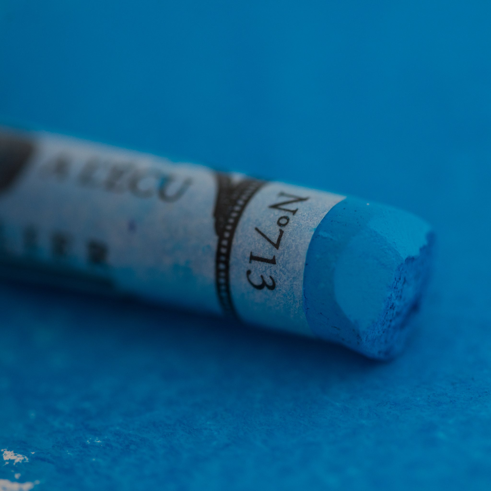  A close-up of a blue Sennelier extra soft pastel on the same coloured background, with the colour information printed on the paper wrap.