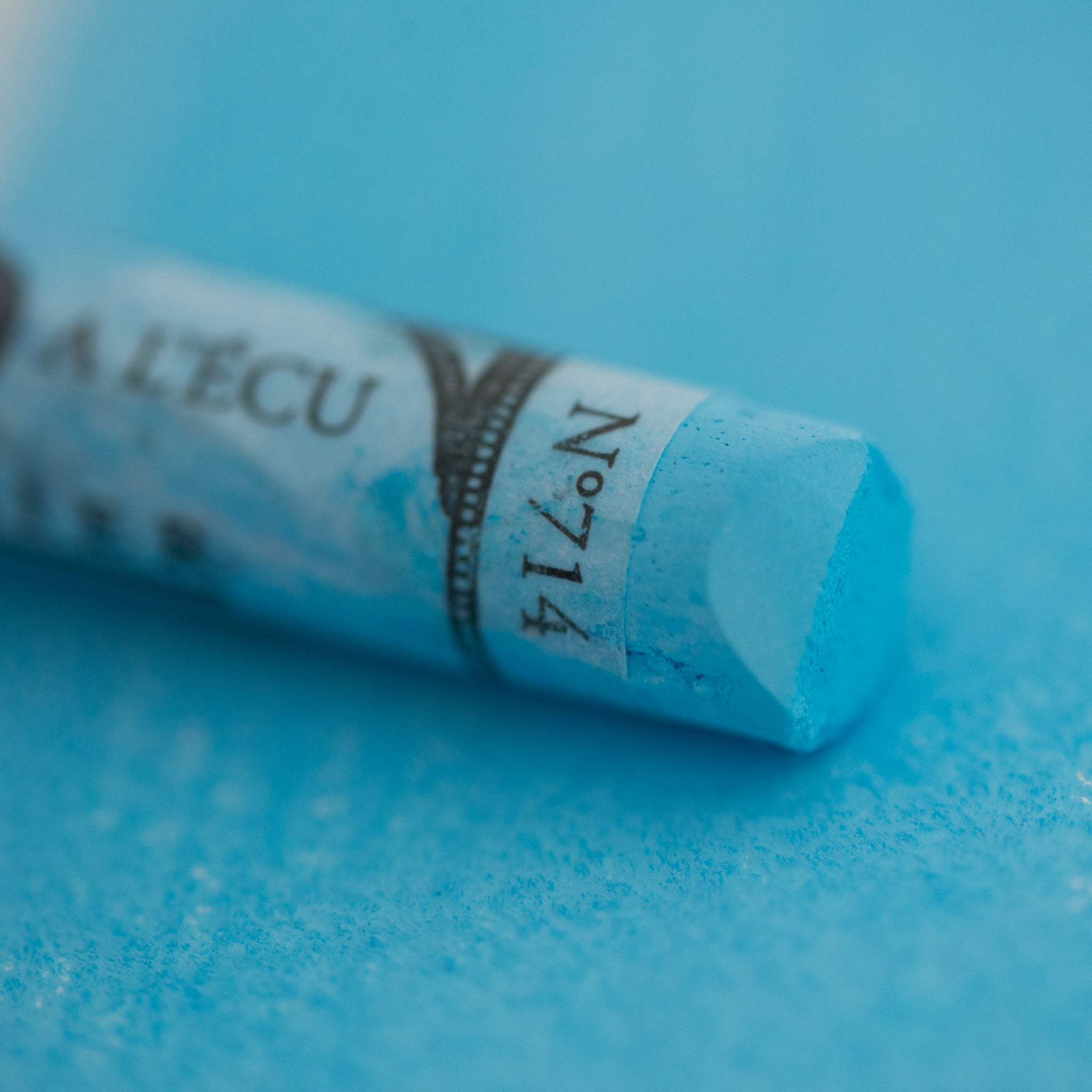  A close-up of a blue Sennelier extra soft pastel on the same coloured background, with the colour information printed on the paper wrap.