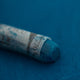  A close-up of a blue Sennelier extra soft pastel on the same coloured background, with the colour information printed on the paper wrap.