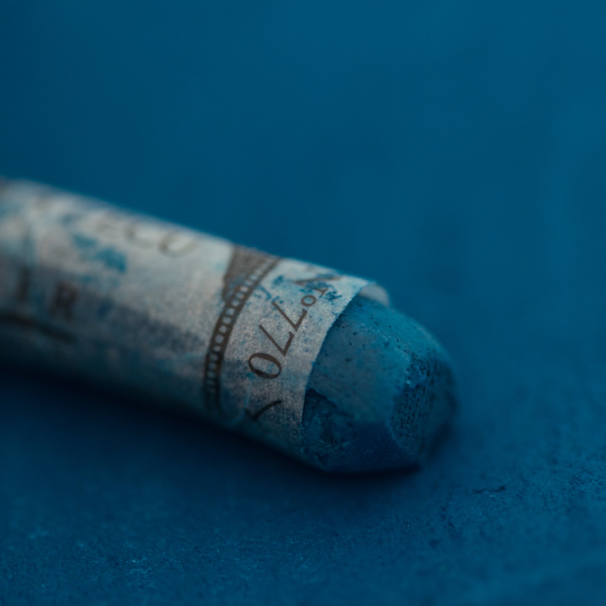  A close-up of a blue Sennelier extra soft pastel on the same coloured background, with the colour information printed on the paper wrap.