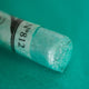 A close-up of an iridescent green Sennelier extra soft pastel. on the same coloured background, with the colour information printed on the paper wrap.