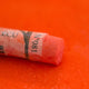 A close-up of a orange Sennelier extra soft pastel on the same coloured background, with the colour information printed on the paper wrap.