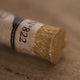 A close-up of an iridescent gold Sennelier extra soft pastel. on the same coloured background, with the colour information printed on the paper wrap.