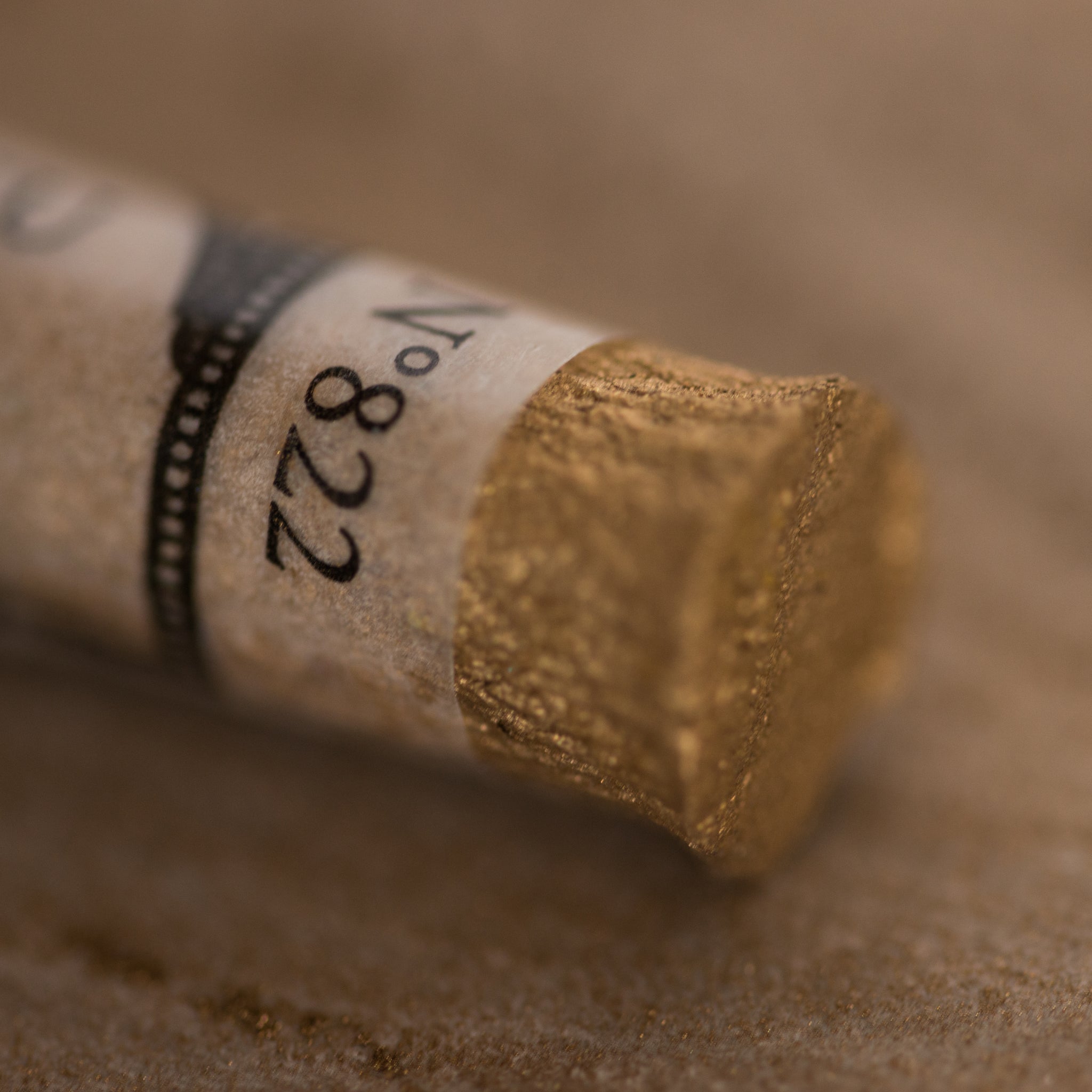 A close-up of an iridescent gold Sennelier extra soft pastel. on the same coloured background, with the colour information printed on the paper wrap.