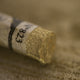 A close-up of an iridescent gold Sennelier extra soft pastel. on the same coloured background, with the colour information printed on the paper wrap.