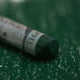 A close-up of a green Sennelier extra soft pastel, on the same coloured background, with the colour information printed on the paper wrap.