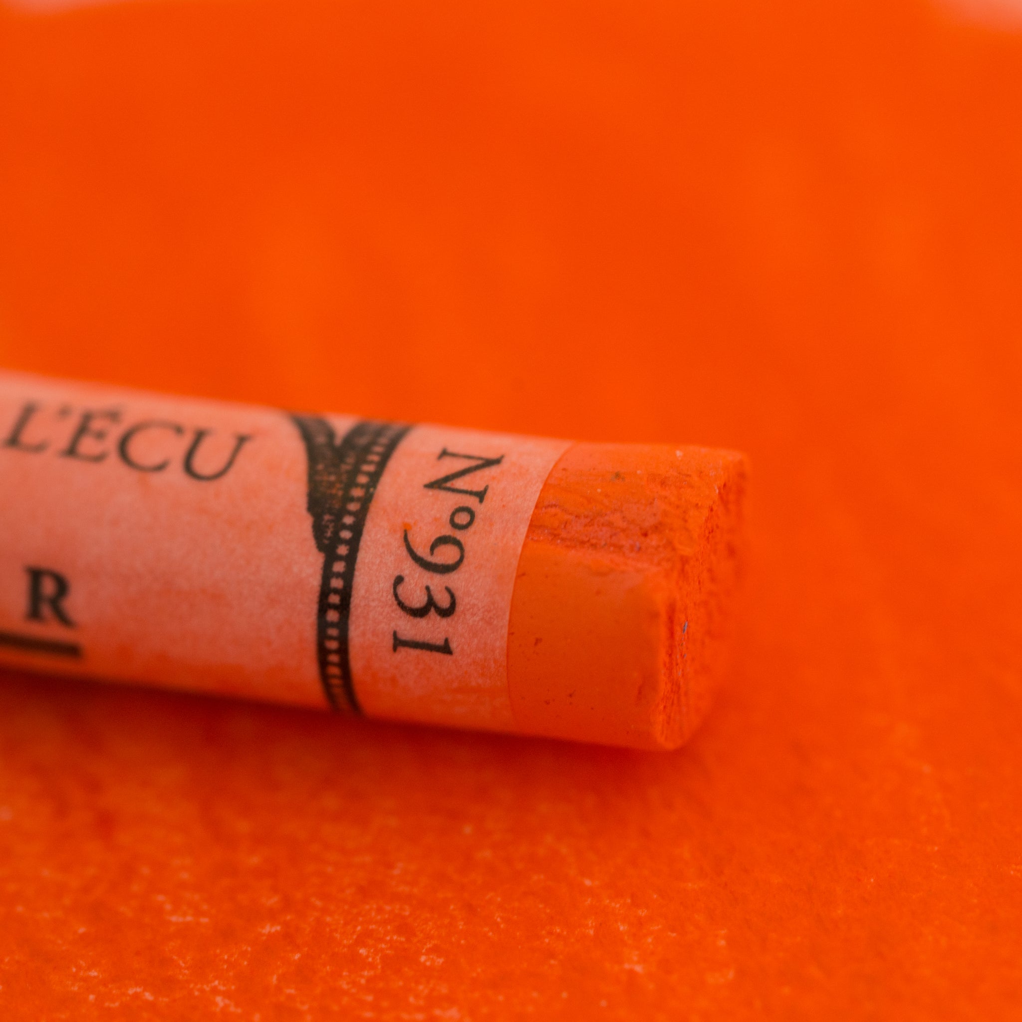 A close-up of a orange Sennelier extra soft pastel on the same coloured background, with the colour information printed on the paper wrap.