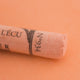 A close-up of a light orange Sennelier extra soft pastel on the same coloured background, with the colour information printed on the paper wrap.