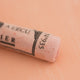 A close-up of a pale orange Sennelier extra soft pastel on the same coloured background, with the colour information printed on the paper wrap.