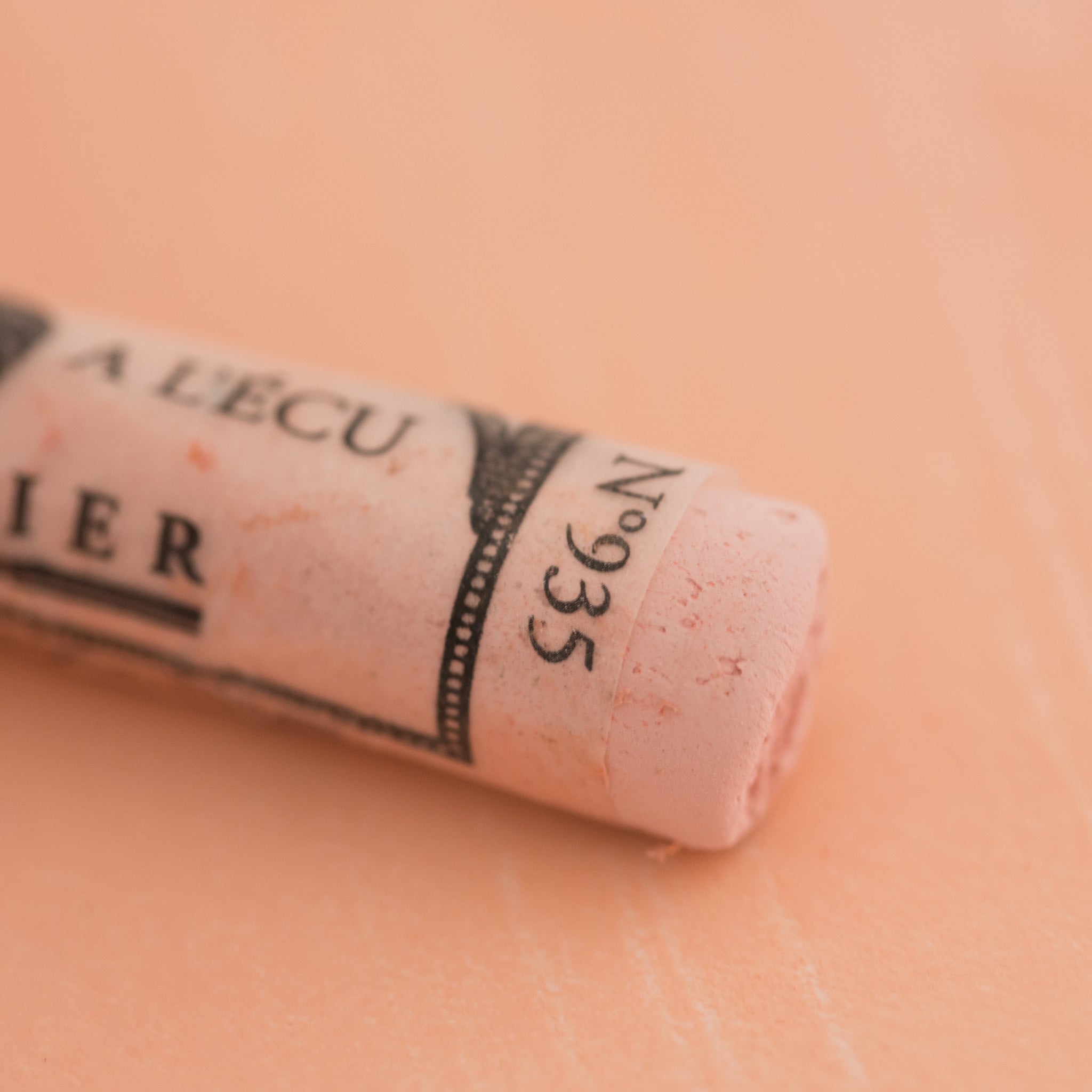 A close-up of a pale orange Sennelier extra soft pastel on the same coloured background, with the colour information printed on the paper wrap.
