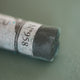 A close-up of a grey Sennelier extra soft pastel. on the same coloured background, with the colour information printed on the paper wrap.