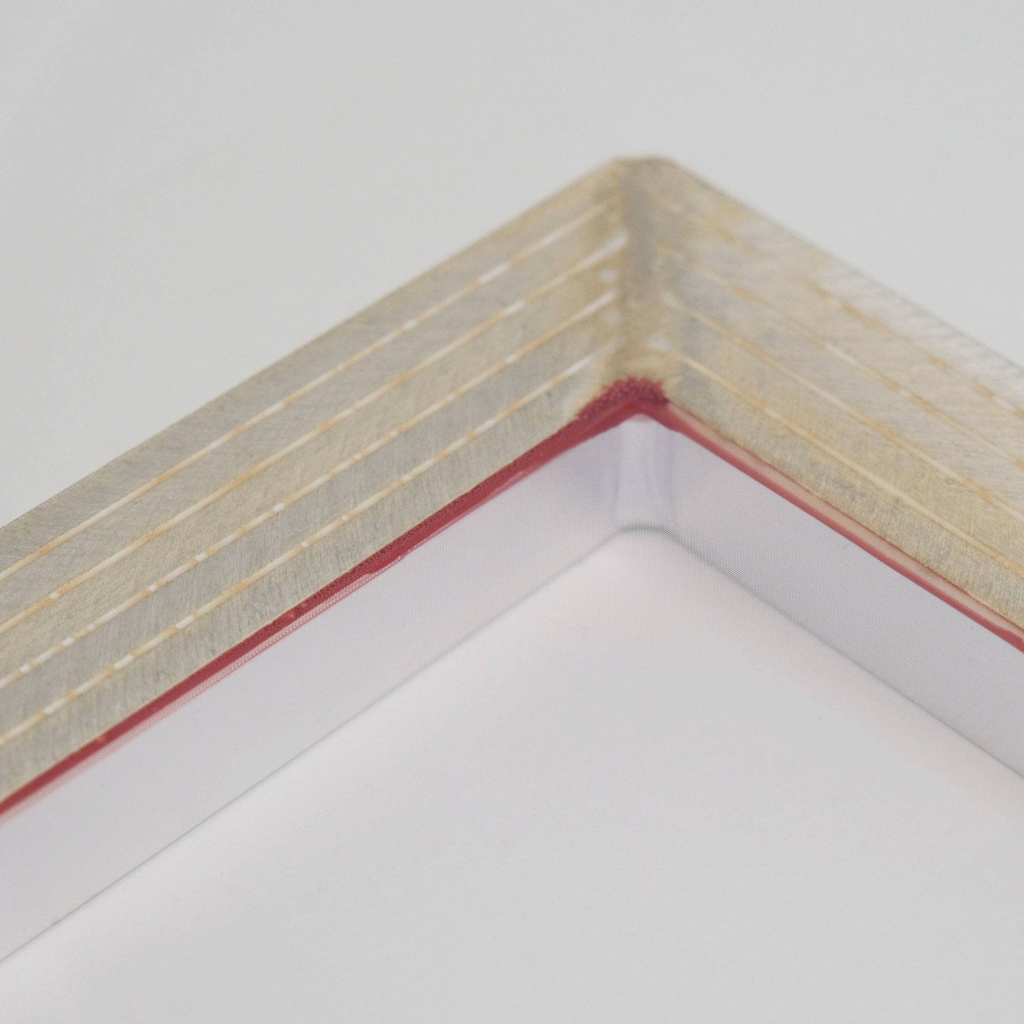 Close-up of an aluminium screen printing frame corner with red and gold inlay and a fine silk mesh on a light background