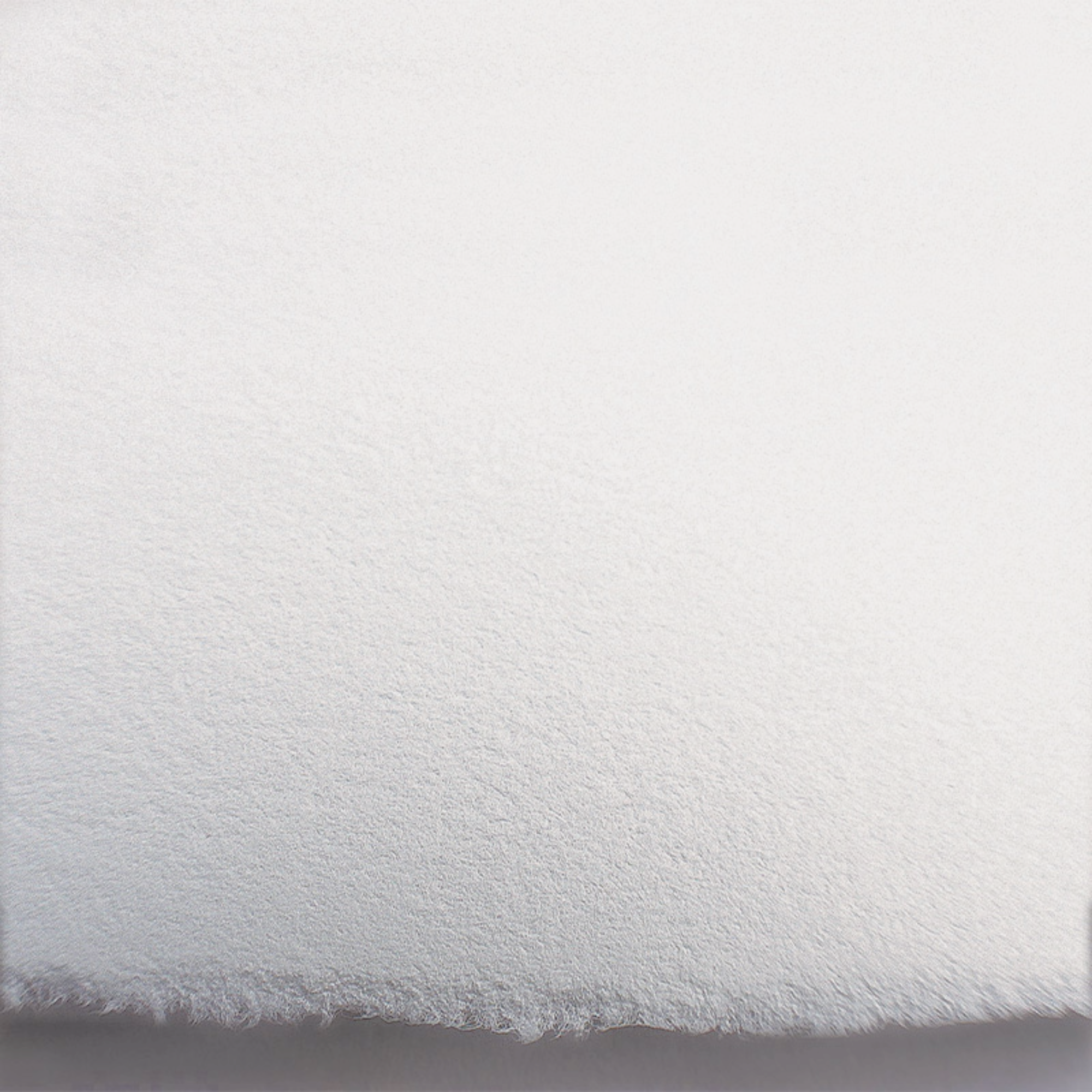Close-up of white paper texture showing a deckled edge on a light grey background