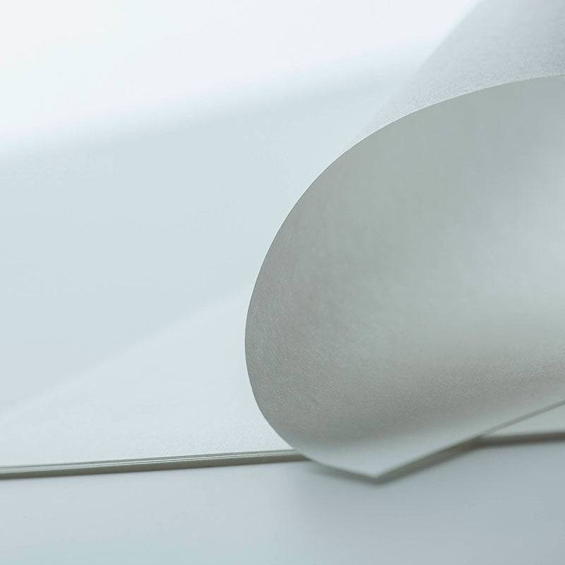 Close up of sheets of a smooth white paper with the top sheet curled back to illustrate the slight transparency of the paper 
