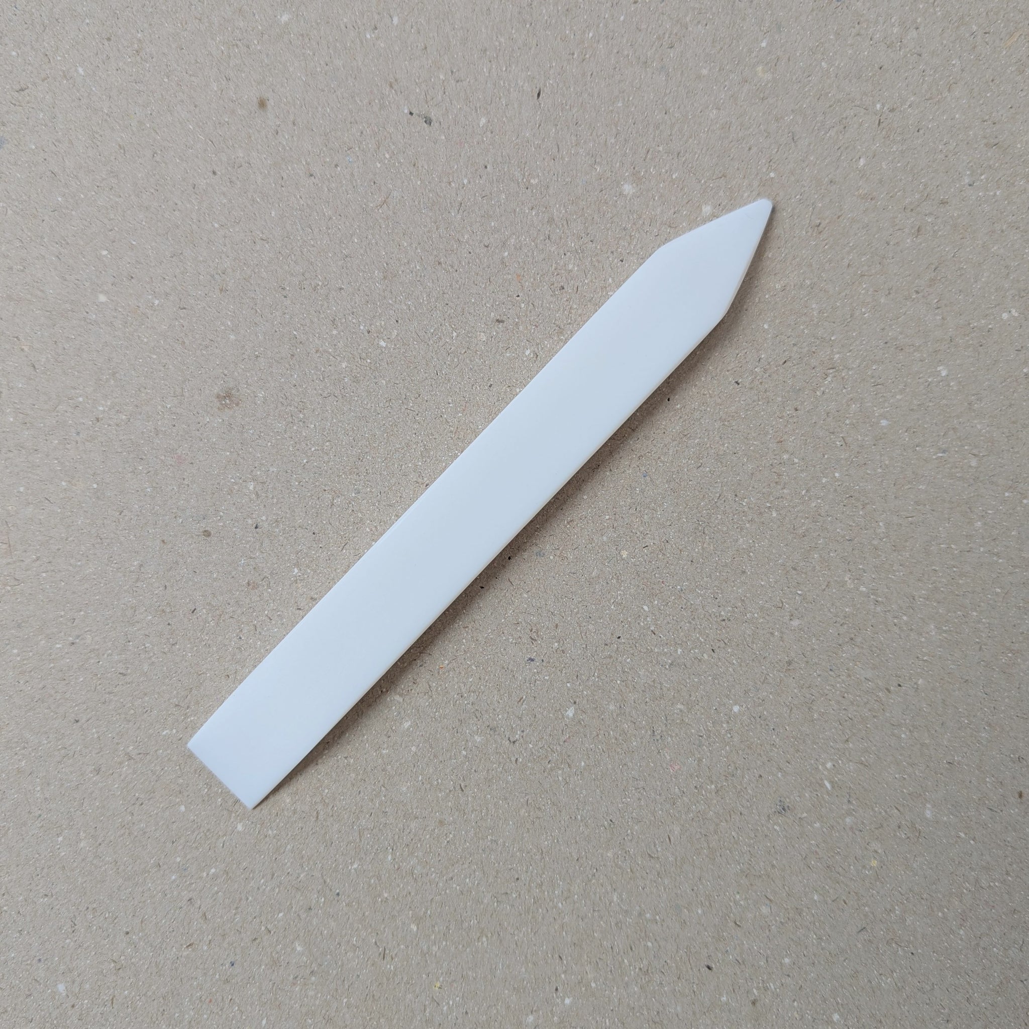 Teflon Bone Folder with one pointed and one slanted edge on a neutral background