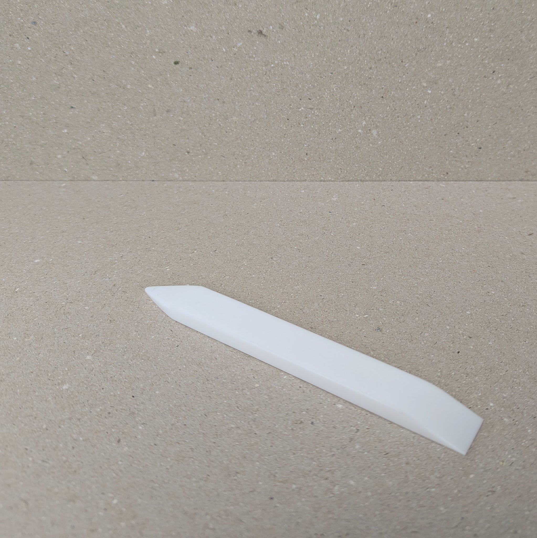 Teflon Bone Folder with one pointed and one slanted edge on a neutral background