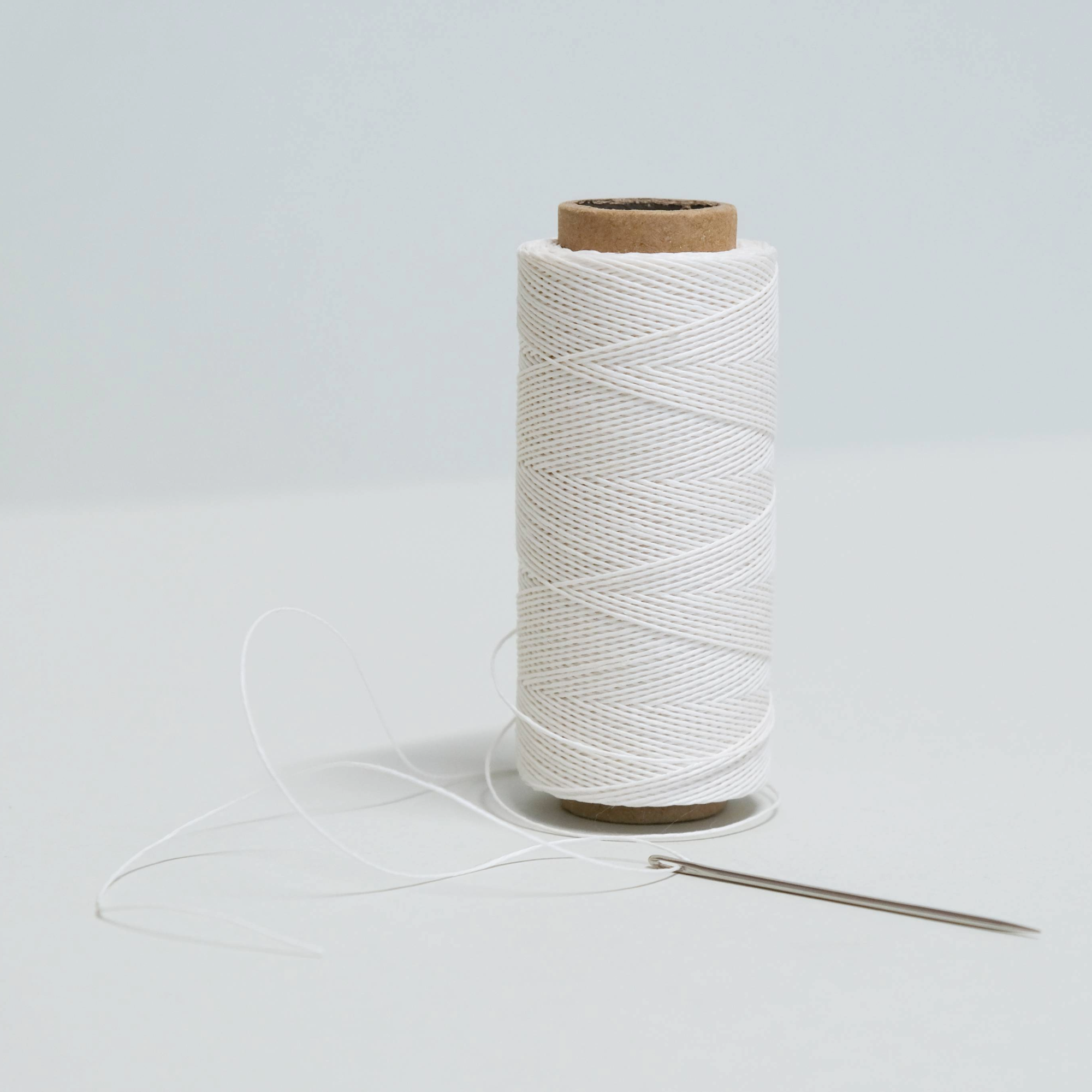 Spool of a smooth white thread with a needle on a light grey background
